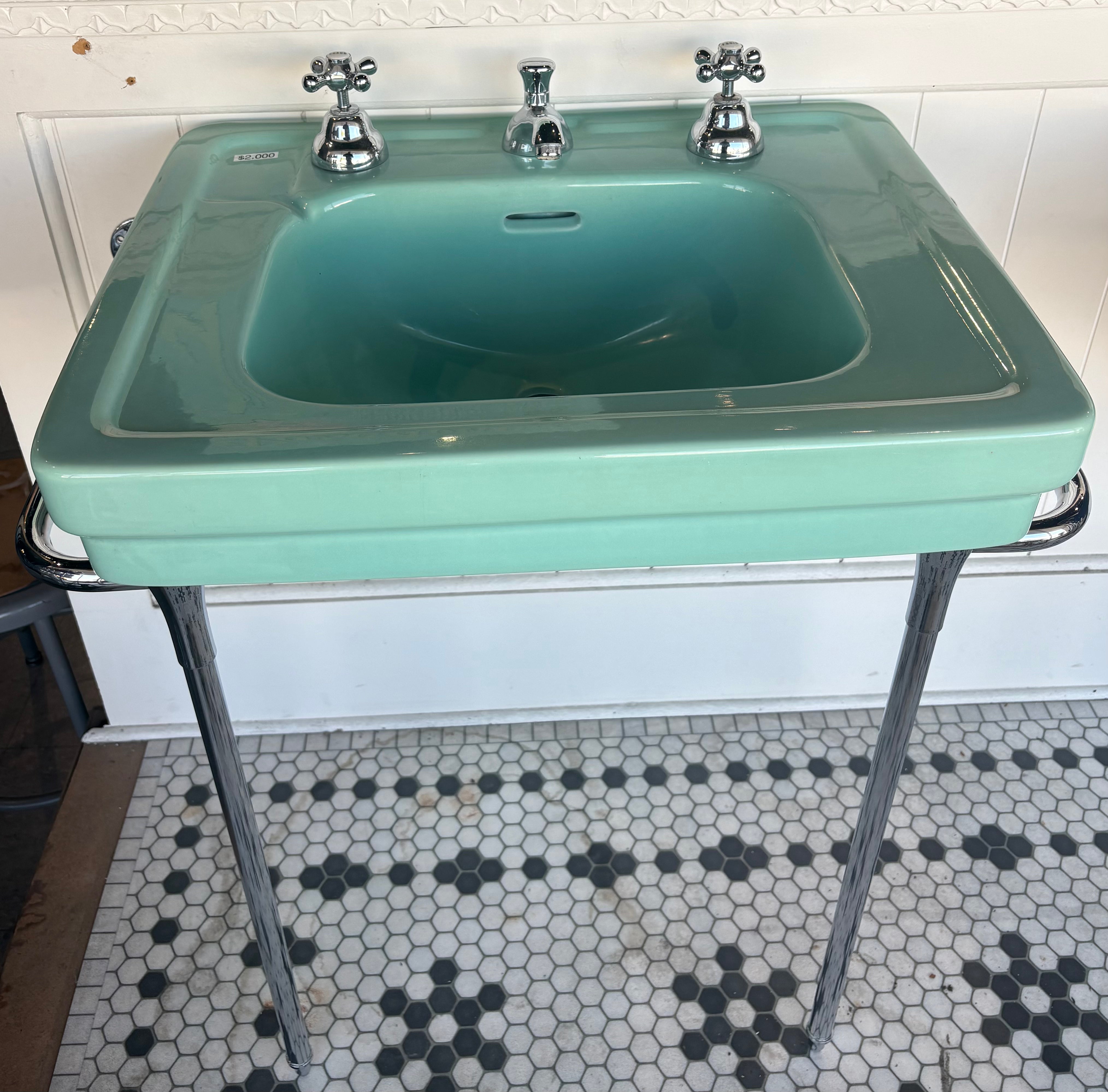 Vintage-style teal sink with metal legs on a tiled bathroom floor.