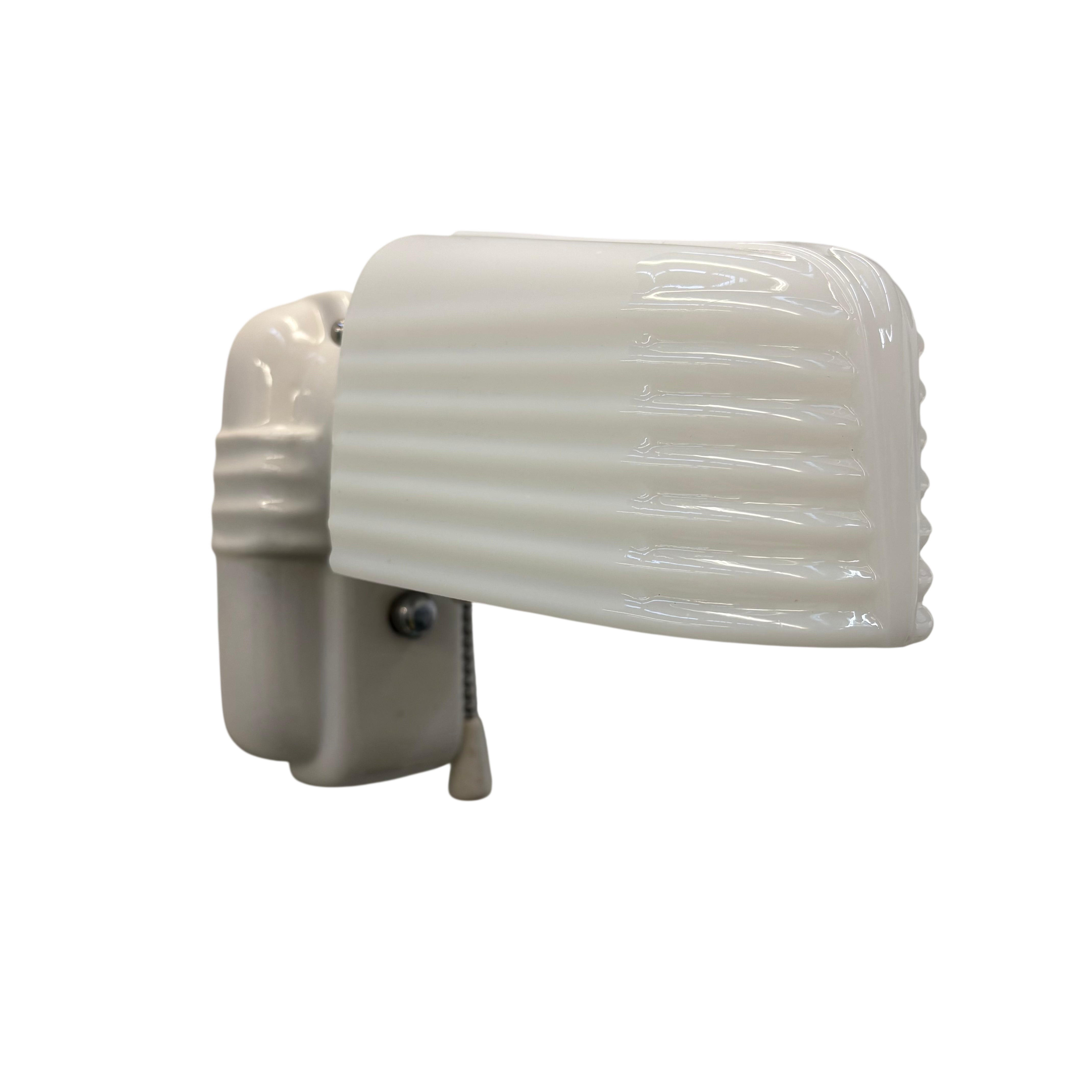 Wall-mounted light fixture with ribbed white glass shade on a white background