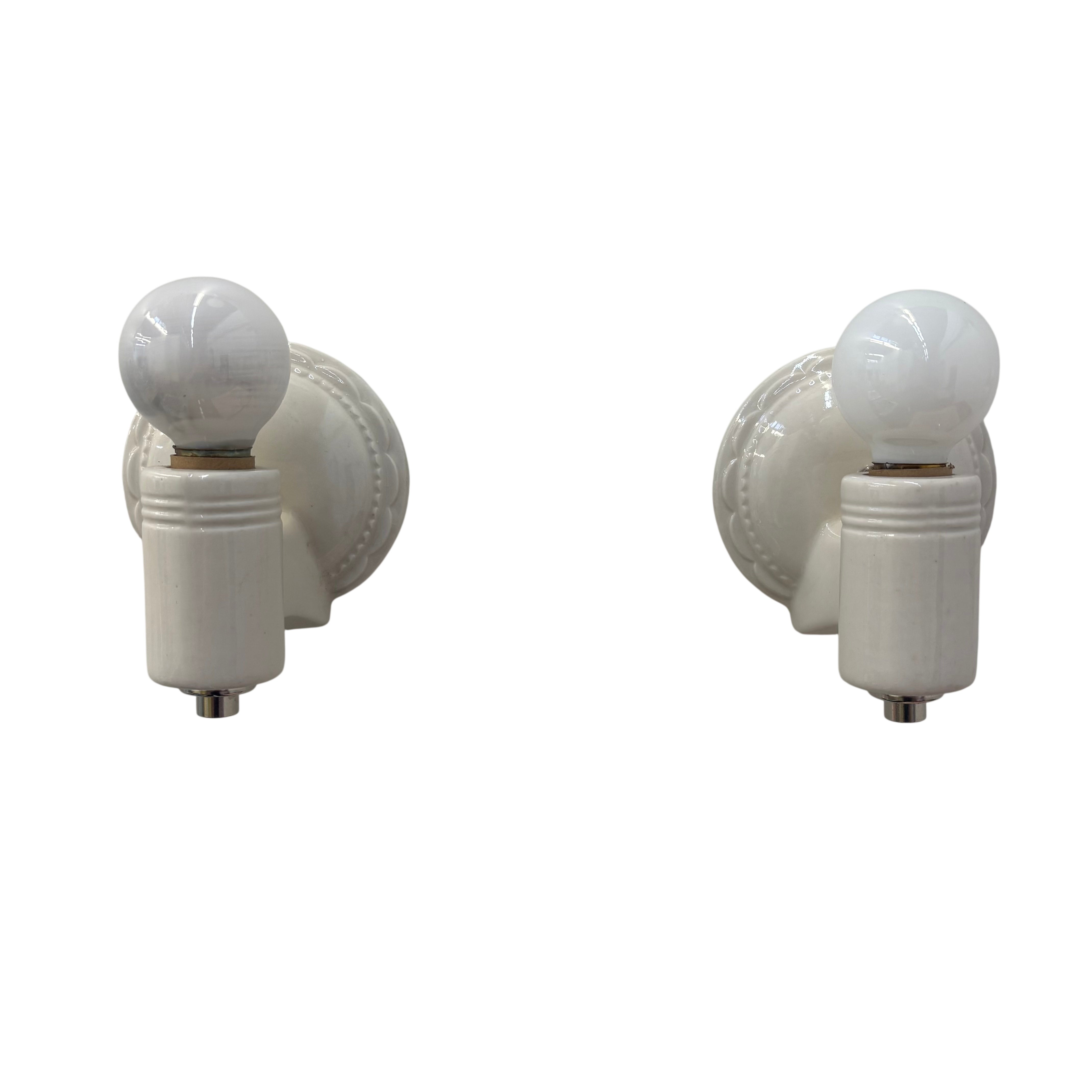 Two white wall sconces with light bulbs on a white background