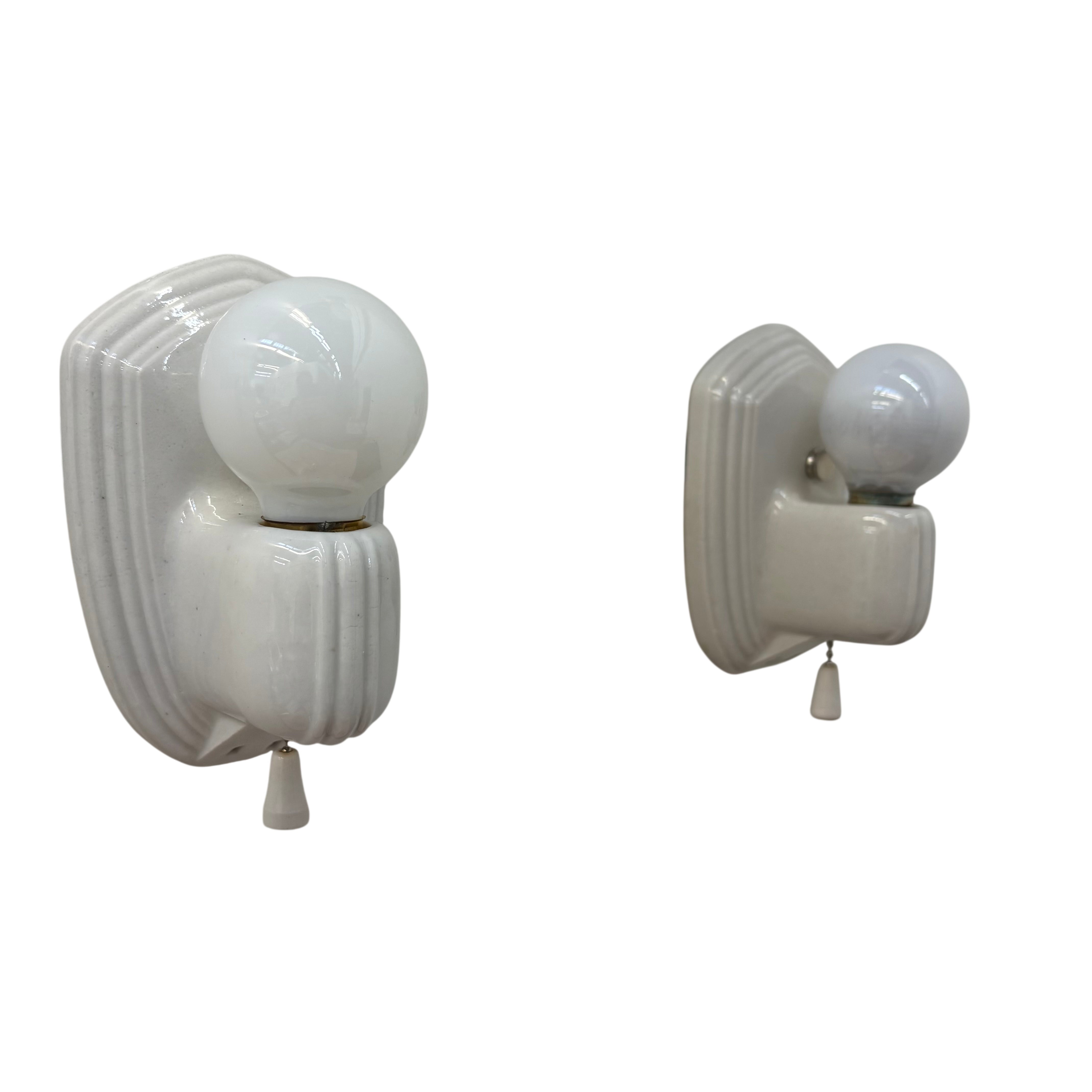 Pair of white wall sconces with glass shades on a white background