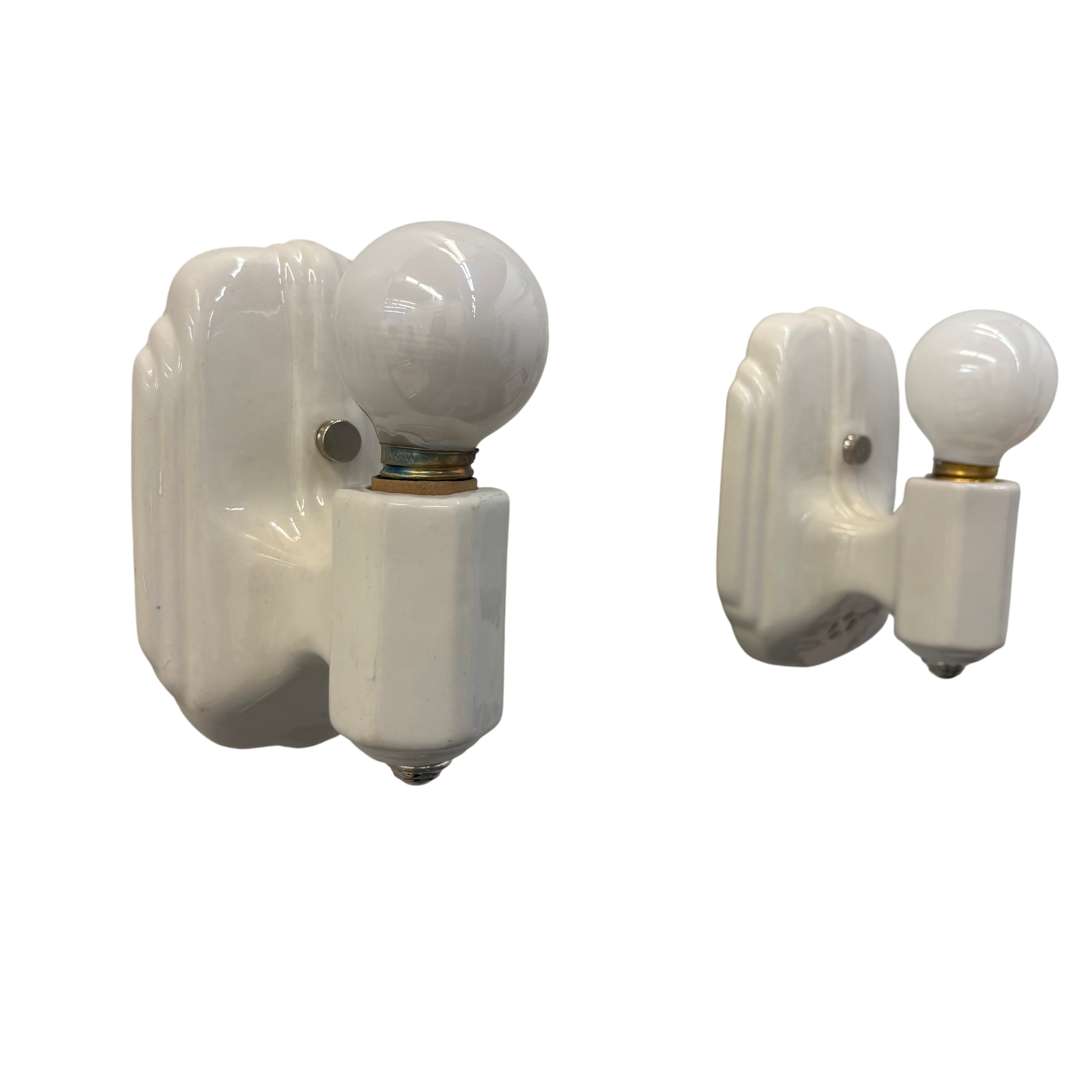 angled two white porcelain sconces with white light bulbs on a white background